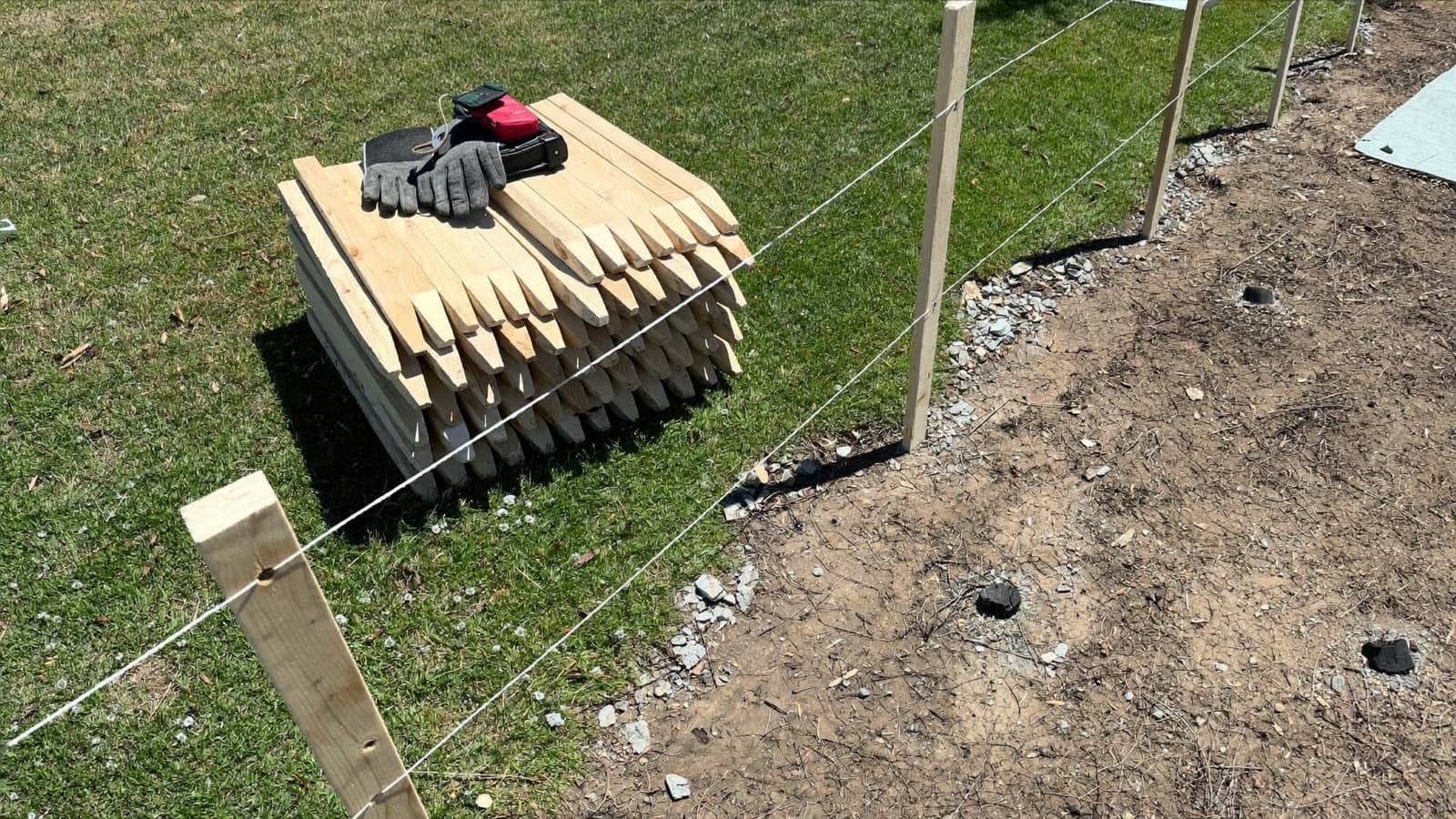 Work gloves resting on a stack of wooden stakes beside a string line marking a new fence line