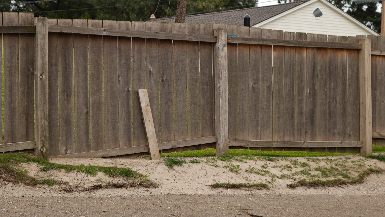 Weathered wood privacy fence leaning along a sandy strip beside a coastal North Carolina road