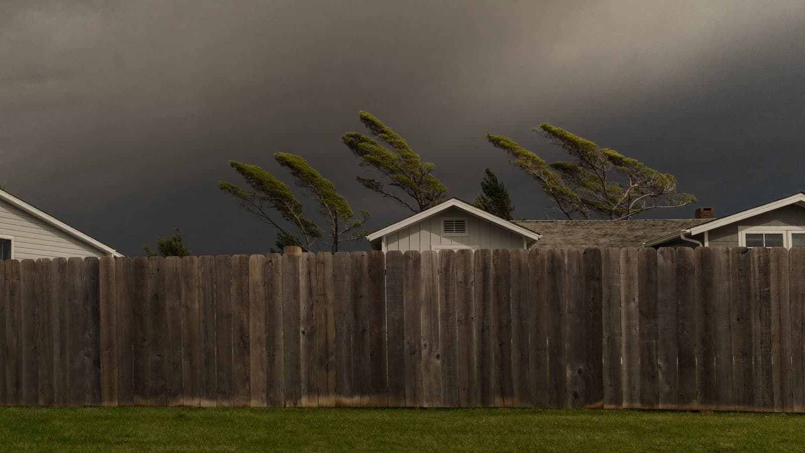Wood privacy fence in a coastal backyard under dark storm clouds rolling in