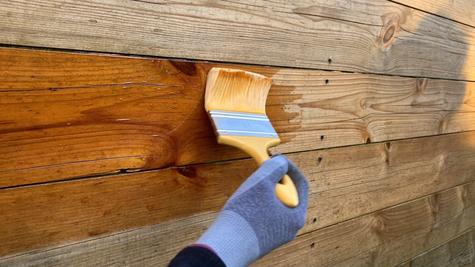 Brush applying semi-transparent stain to wood fence boards