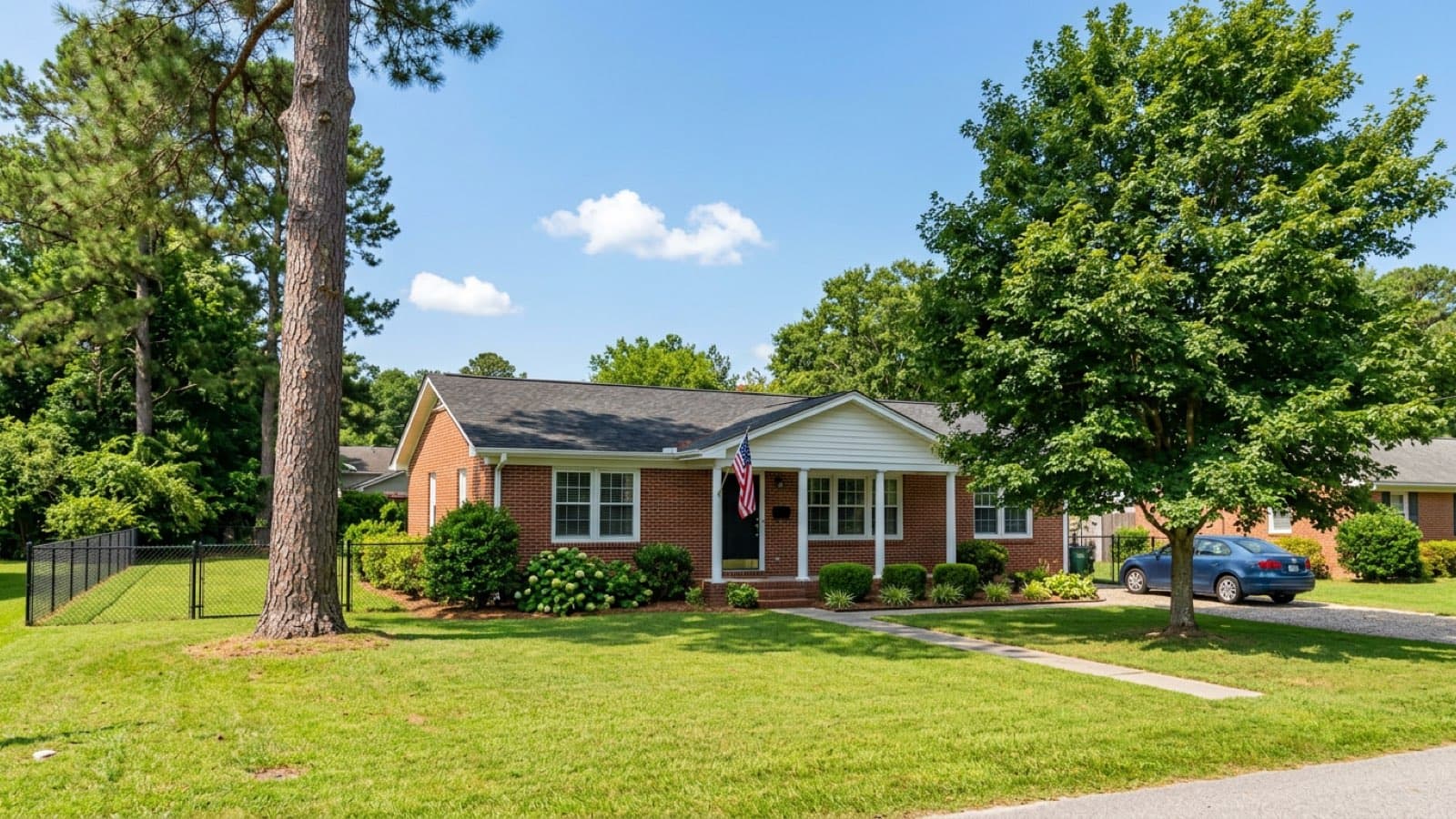 Fenced backyard of a brick ranch home with an American flag on the porch