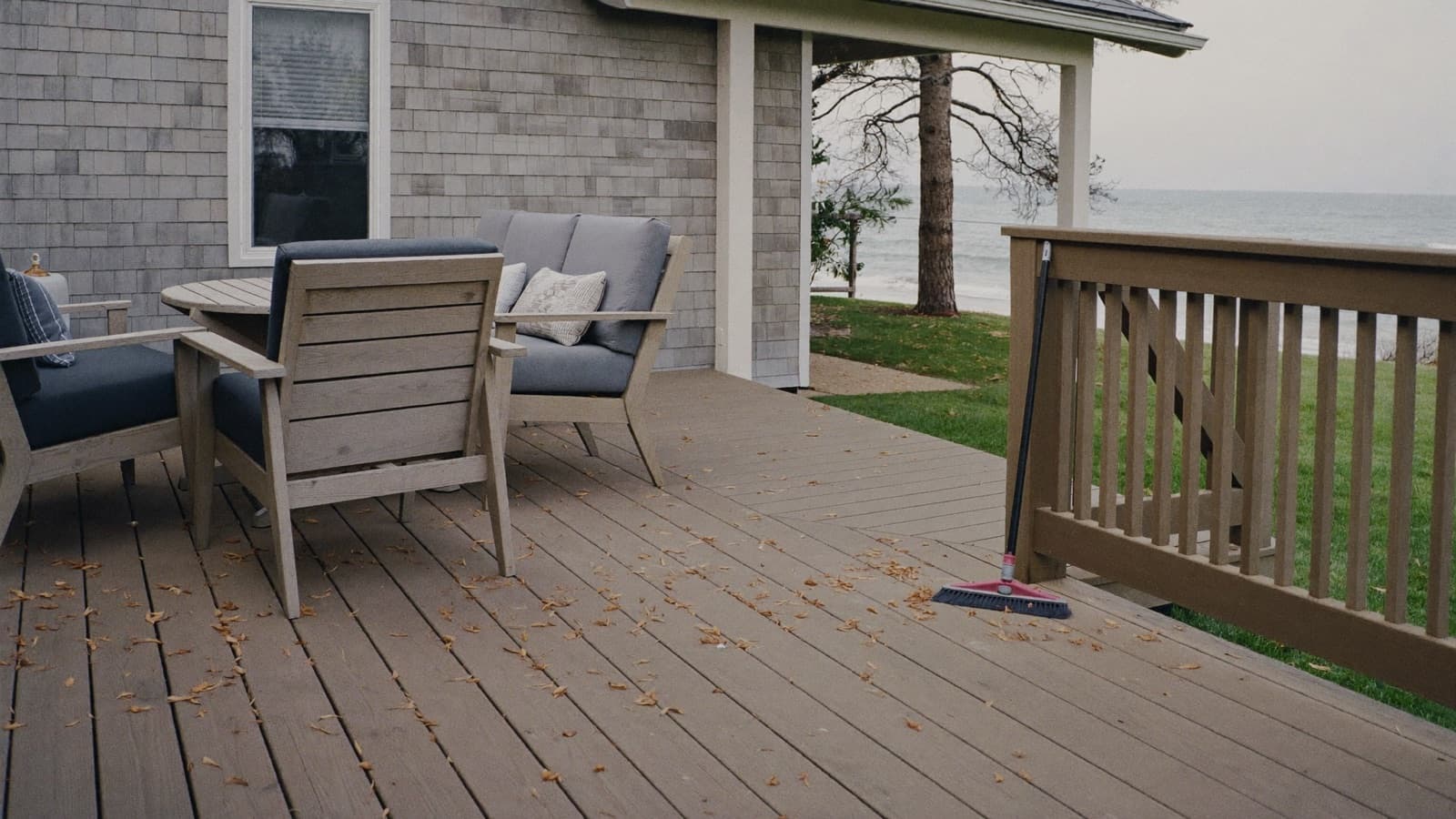 Composite deck with outdoor seating beside a coastal home, broom resting against the railing