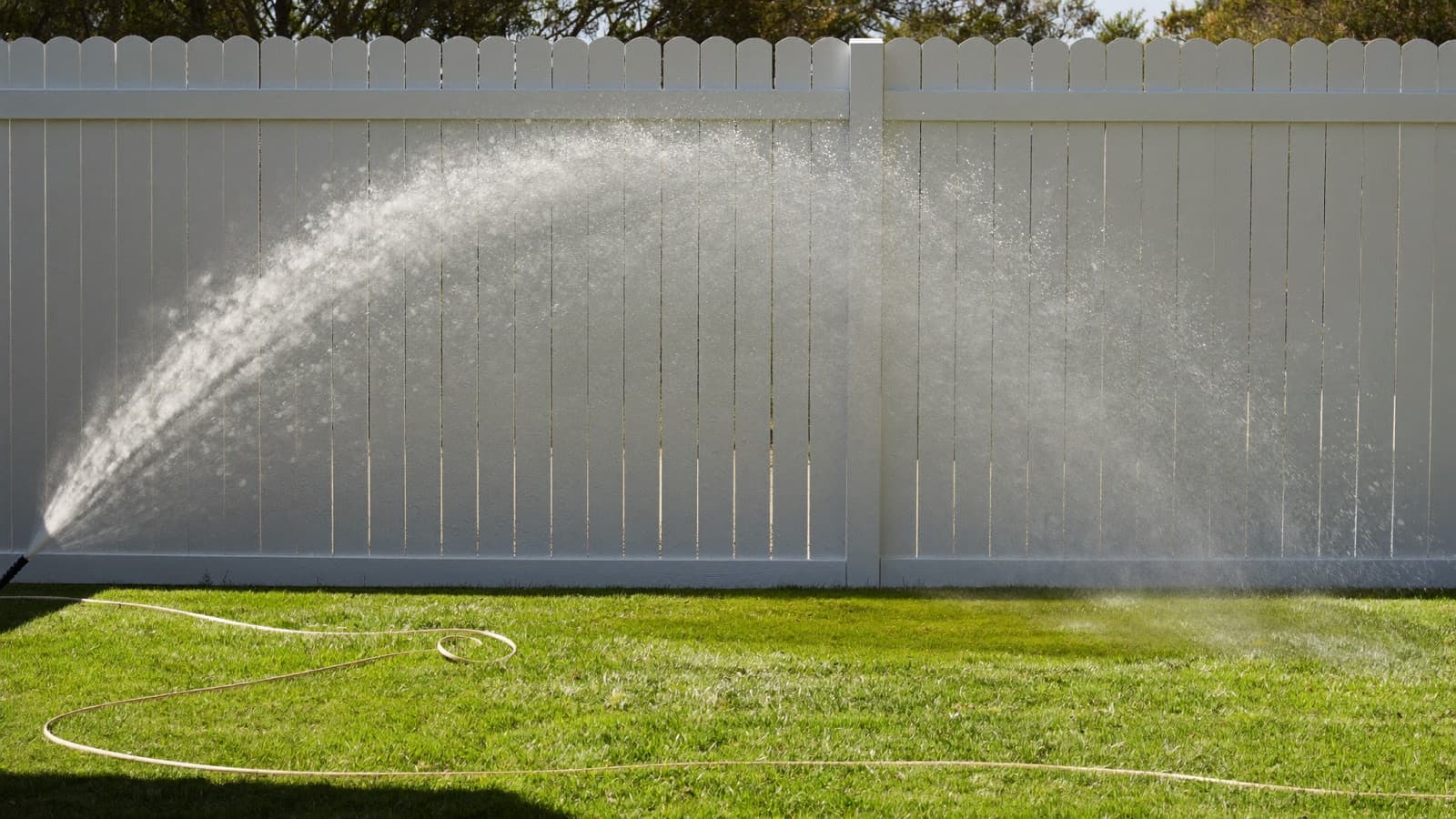 White vinyl privacy fence being rinsed clean with a garden hose