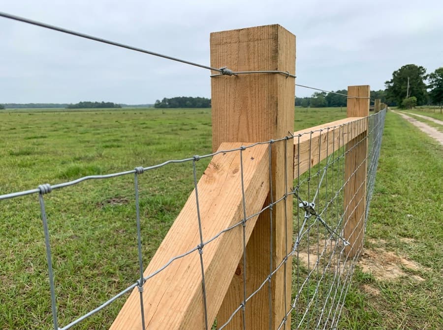Braced wooden corner assembly with woven wire field fencing stretched tight along a pasture
